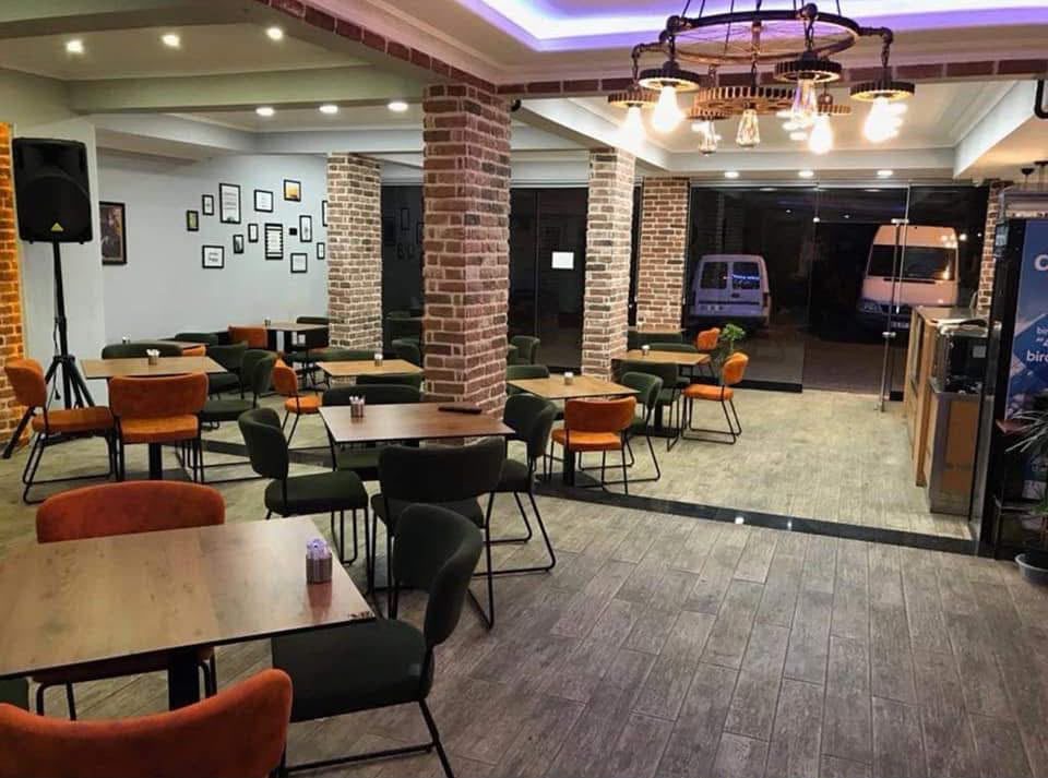 Tuğla sütunlu, turuncu ve yeşil sandalyeli geniş salon